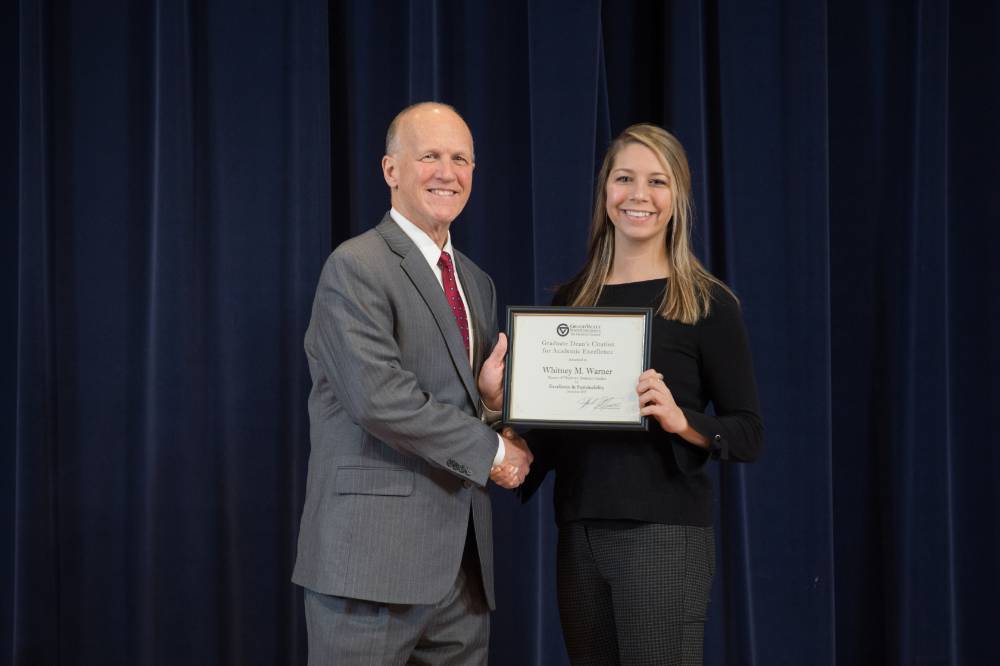 Dean Potteiger and graduate student posing with an award on stage